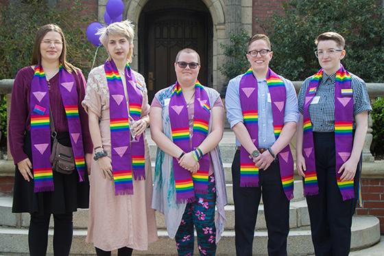 图为一群英国波胆网站的学生穿着印有彩虹LGBTQ+图案的毕业礼服, posing together for a photo. 